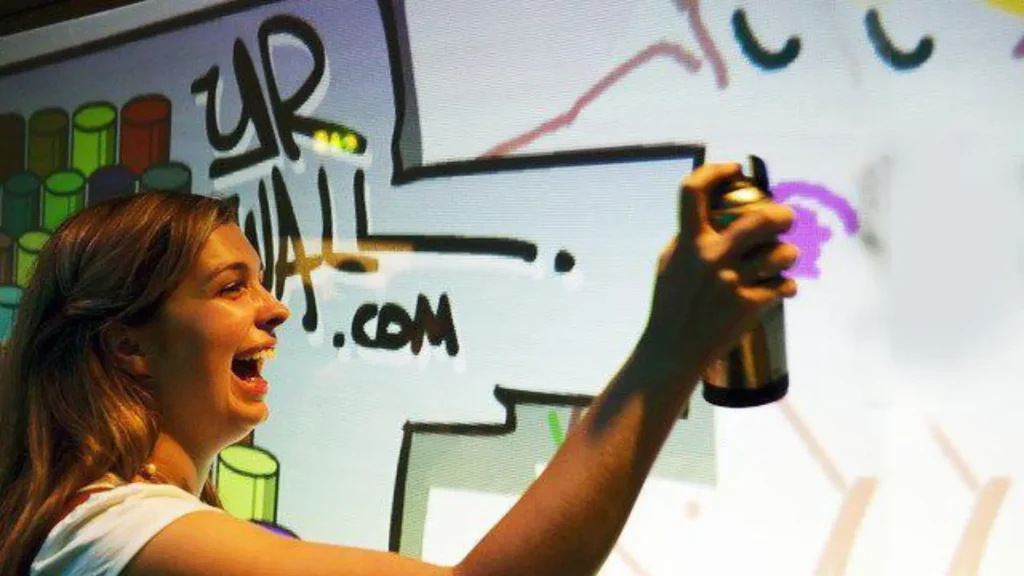 Participante dessinant en direct sur un mur interactif digital lors d’un événement créatif avec bombe graphique virtuelle