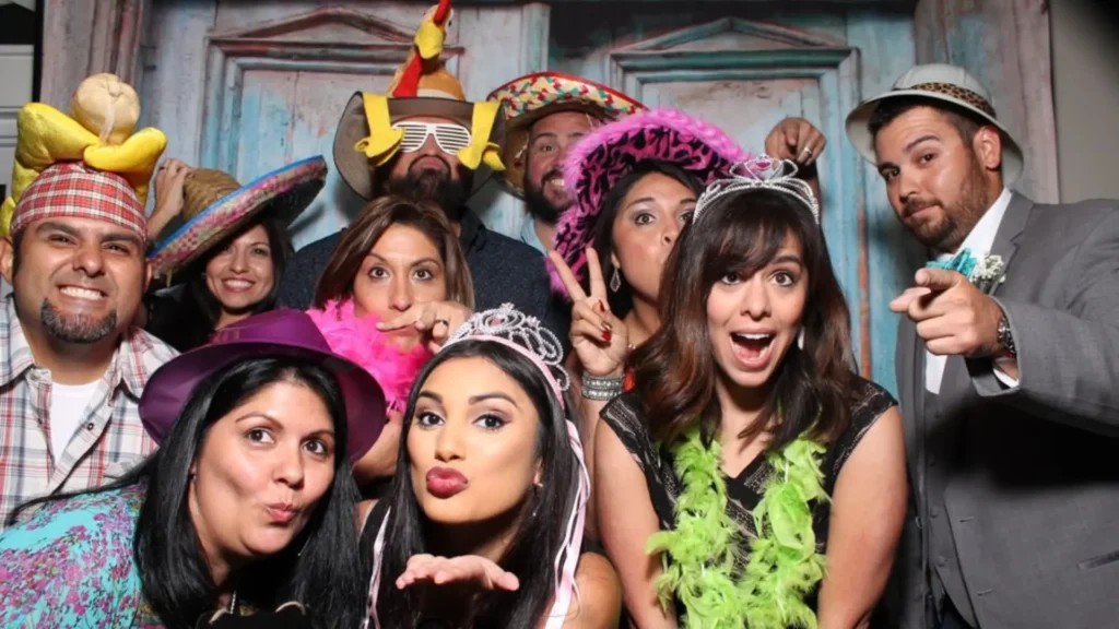 Invités déguisés posant devant un photobooth lors d’un mariage ou anniversaire avec accessoires festifs